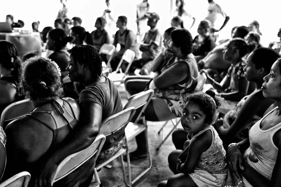 Assemblée de femmes et d'enfants assis sur des chaises pliantes sous un abri, noir et blanc