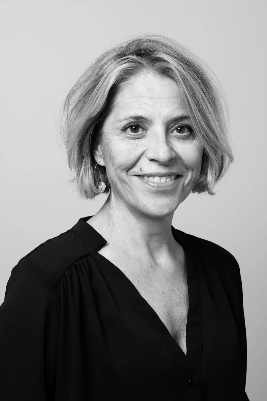 Femme aux cheveux blonds courts en blouse noire souriant, cadrage buste, noir et blanc