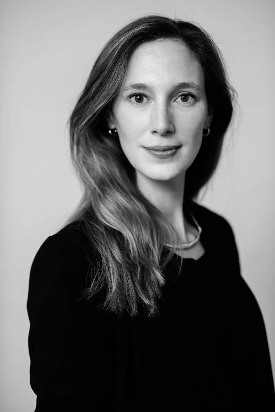 Femme aux longs cheveux clairs en haut noir, cadrage buste, fond clair, noir et blanc