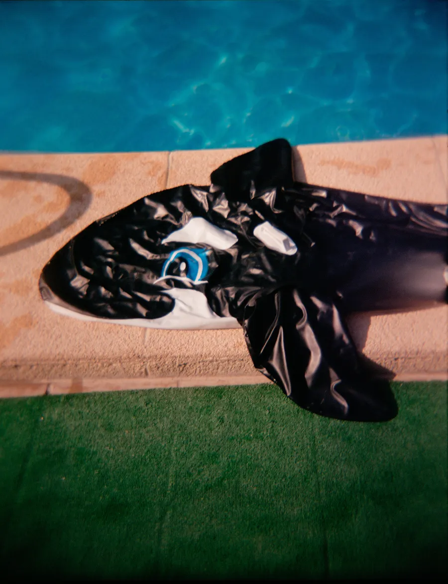 Bouée gonflable en forme d'orque dégonflée au bord d'une piscine, gazon synthétique