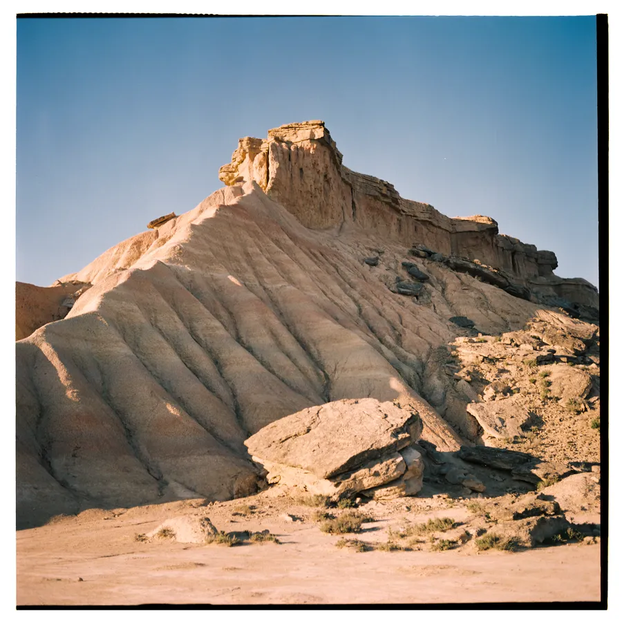 Butte de terre ocre aux flancs ravinés surmontée d'une corniche rocheuse, ciel bleu profond
