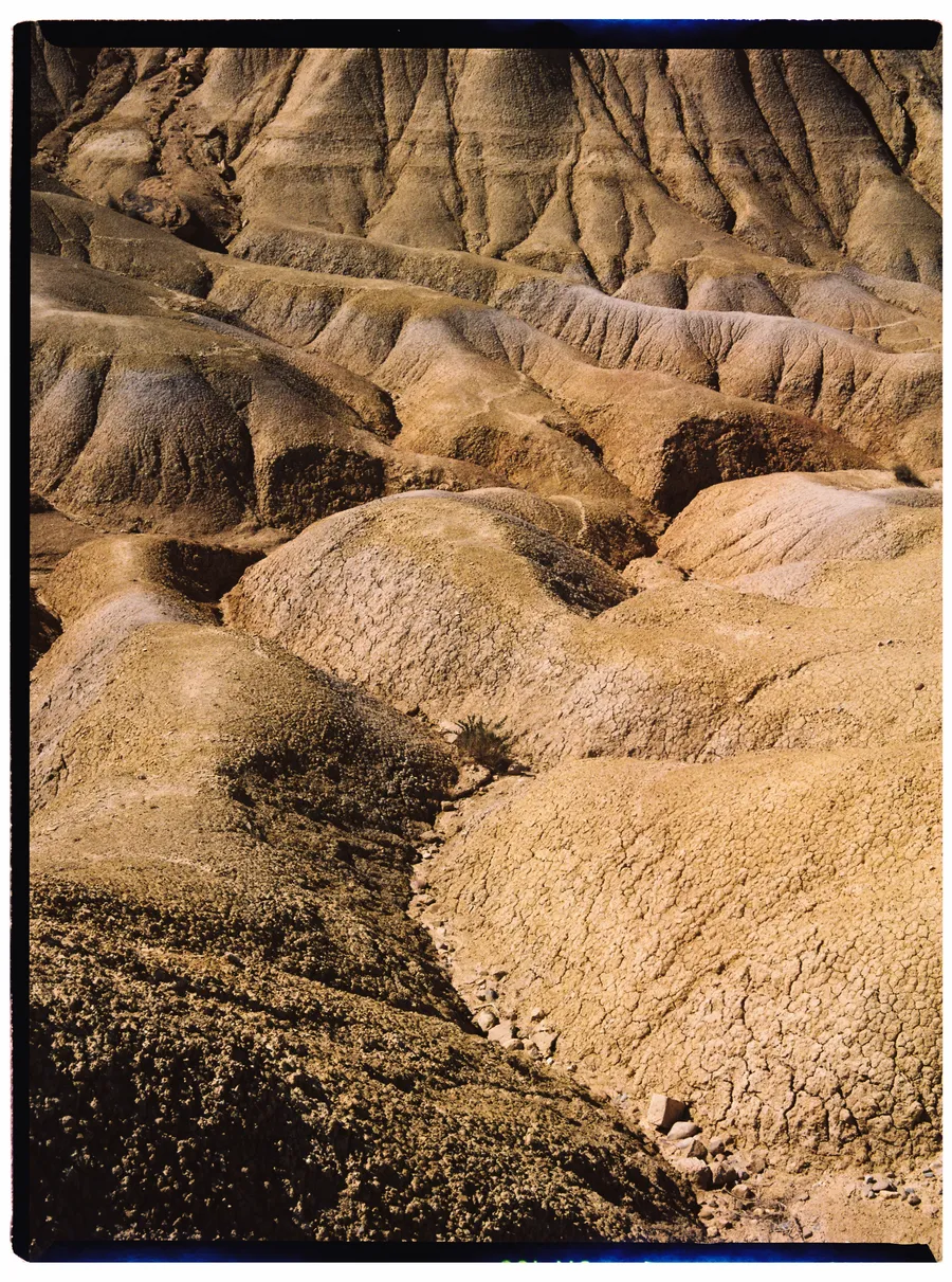 Reliefs d'argile ocre érodés en plis et ravines, sol craquelé au premier plan