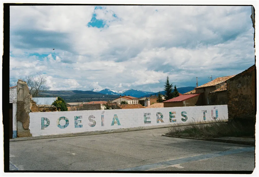 Mur peint des lettres « POESÍA ERES TÚ » dans un village, montagnes enneigées au loin
