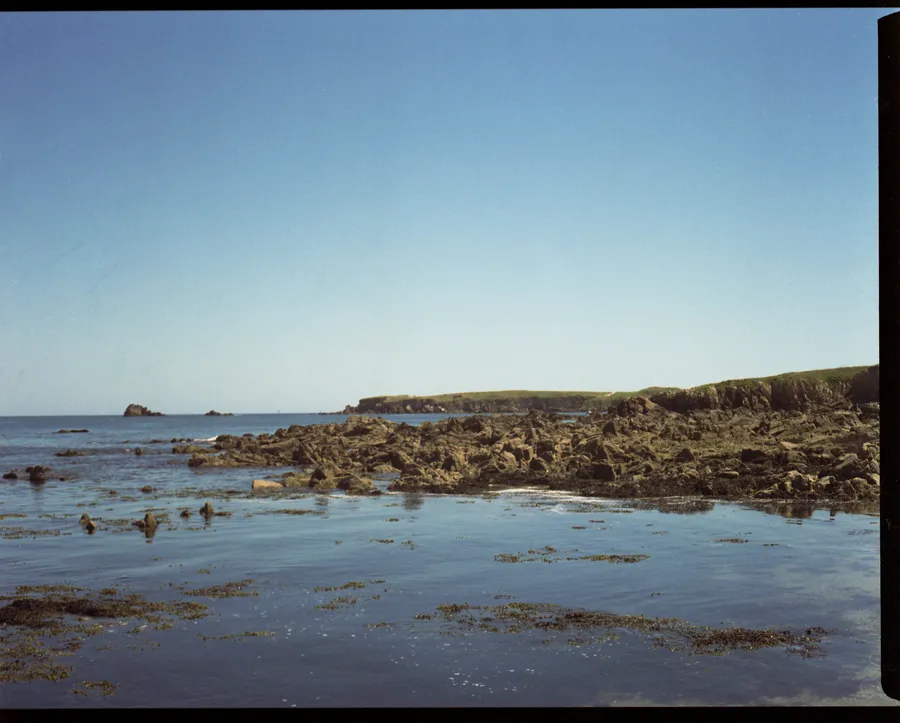 Côte rocheuse à marée basse, eau calme et falaises herbeuses sous un ciel bleu