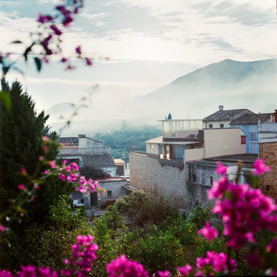 Village aux toits de tuiles vu à travers des bougainvilliers roses, montagnes brumeuses au fond