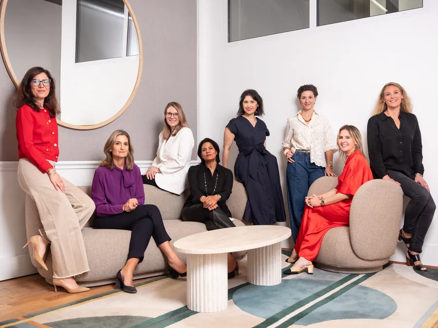 Neuf femmes réunies autour d'un canapé et de tables basses dans un salon de bureau