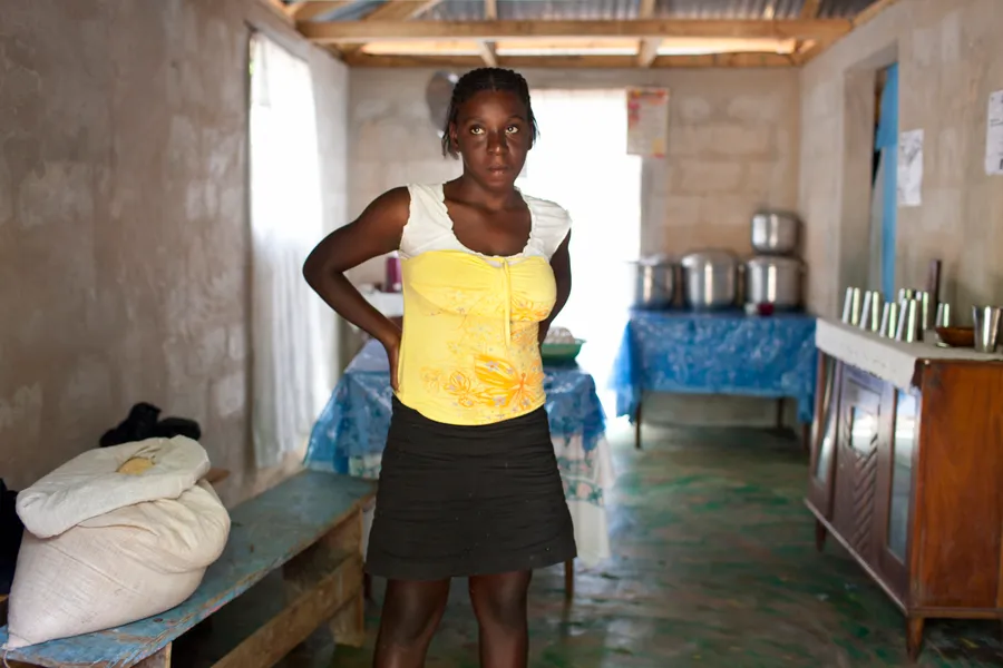 Jeune femme debout, main sur la hanche, dans une cuisine collective aux marmites alignées
