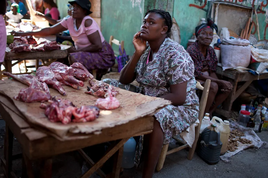 Vendeuse assise derrière un étal de viande sur un marché de rue, autres marchandes derrière