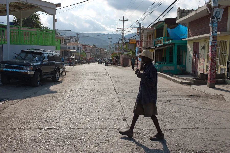 Personne au chapeau traversant une rue commerçante, montagnes et fils électriques au loin