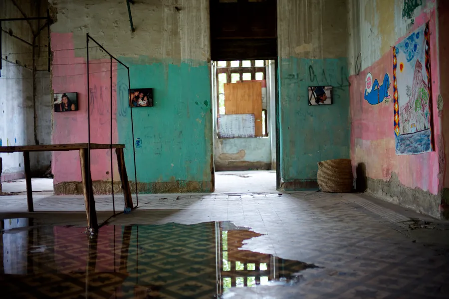 Salle abandonnée aux murs roses et verts, photos accrochées et flaque d'eau reflétant le carrelage