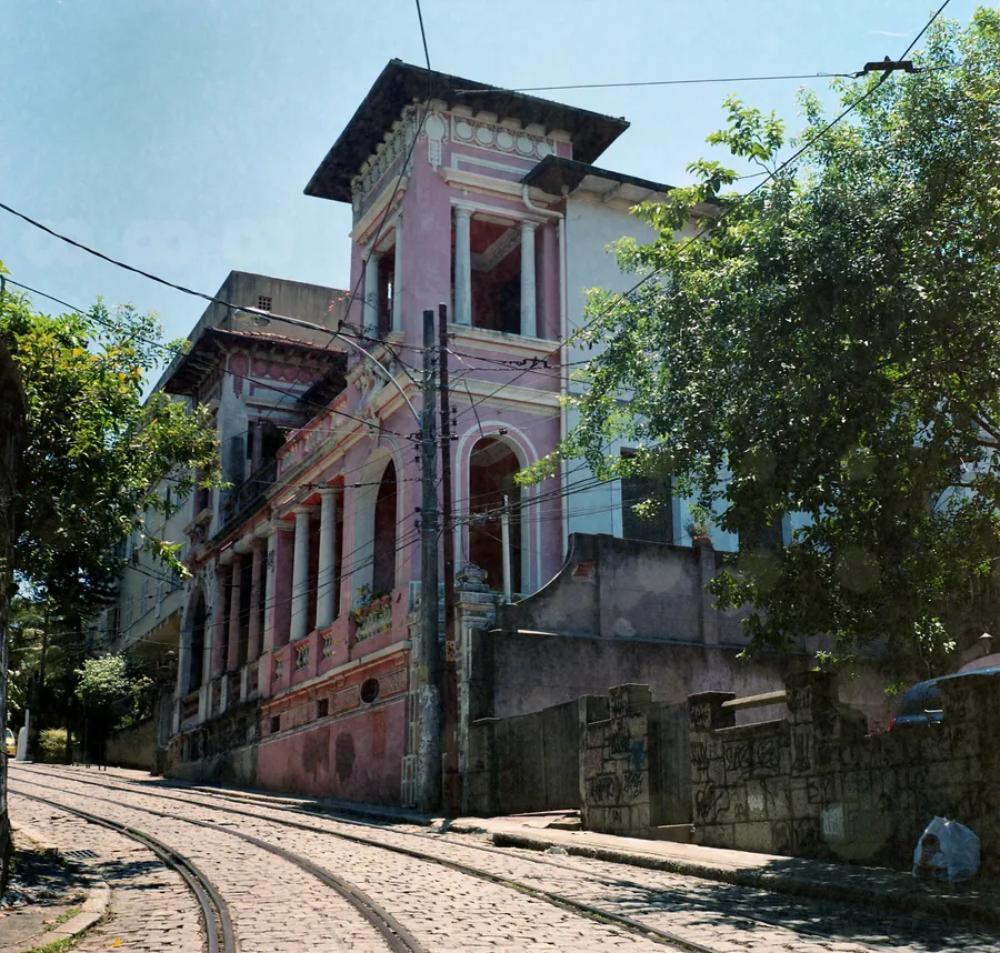 Bâtisse ancienne rose à colonnes au coin d'une rue pavée aux rails de tramway