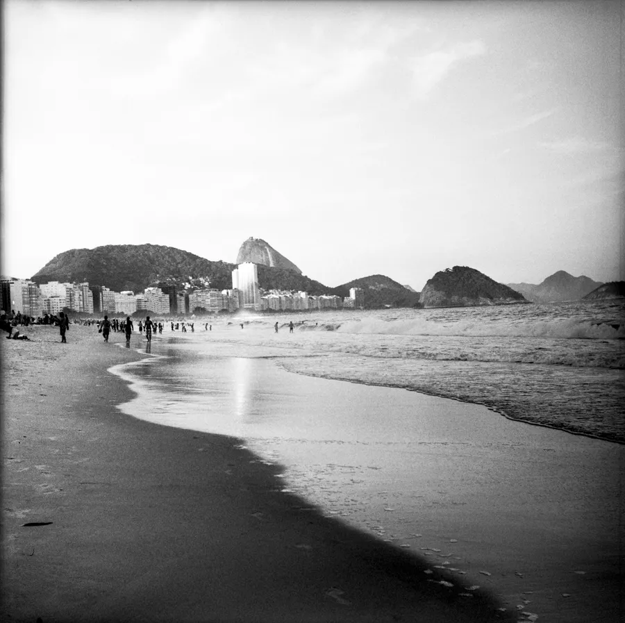 Plage animée en noir et blanc, immeubles et pain de sucre se découpant à l'horizon