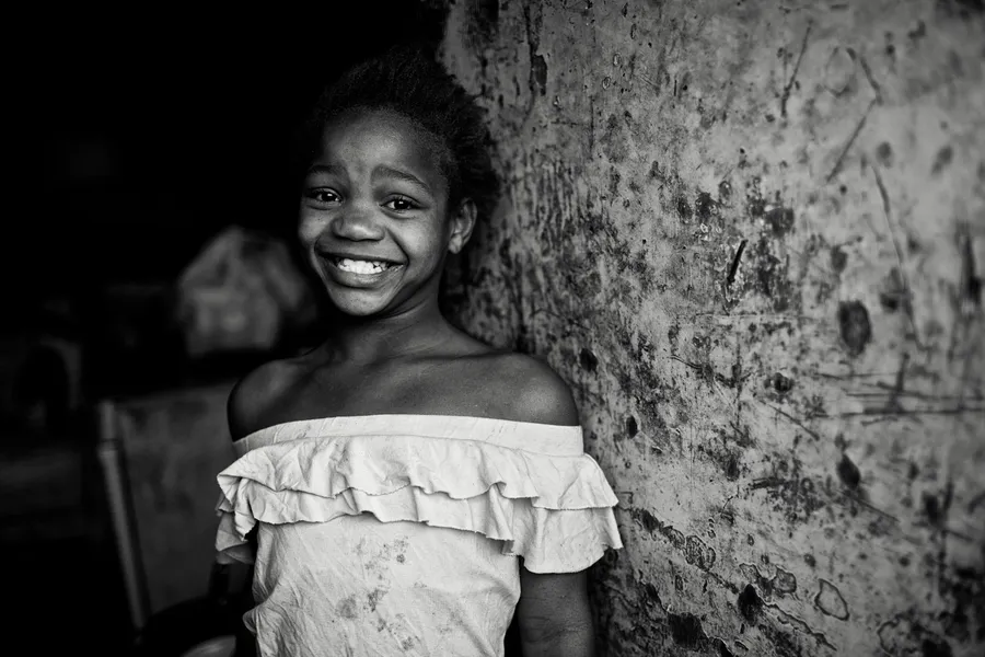 Fillette souriante en haut à volants adossée à un mur écaillé, noir et blanc