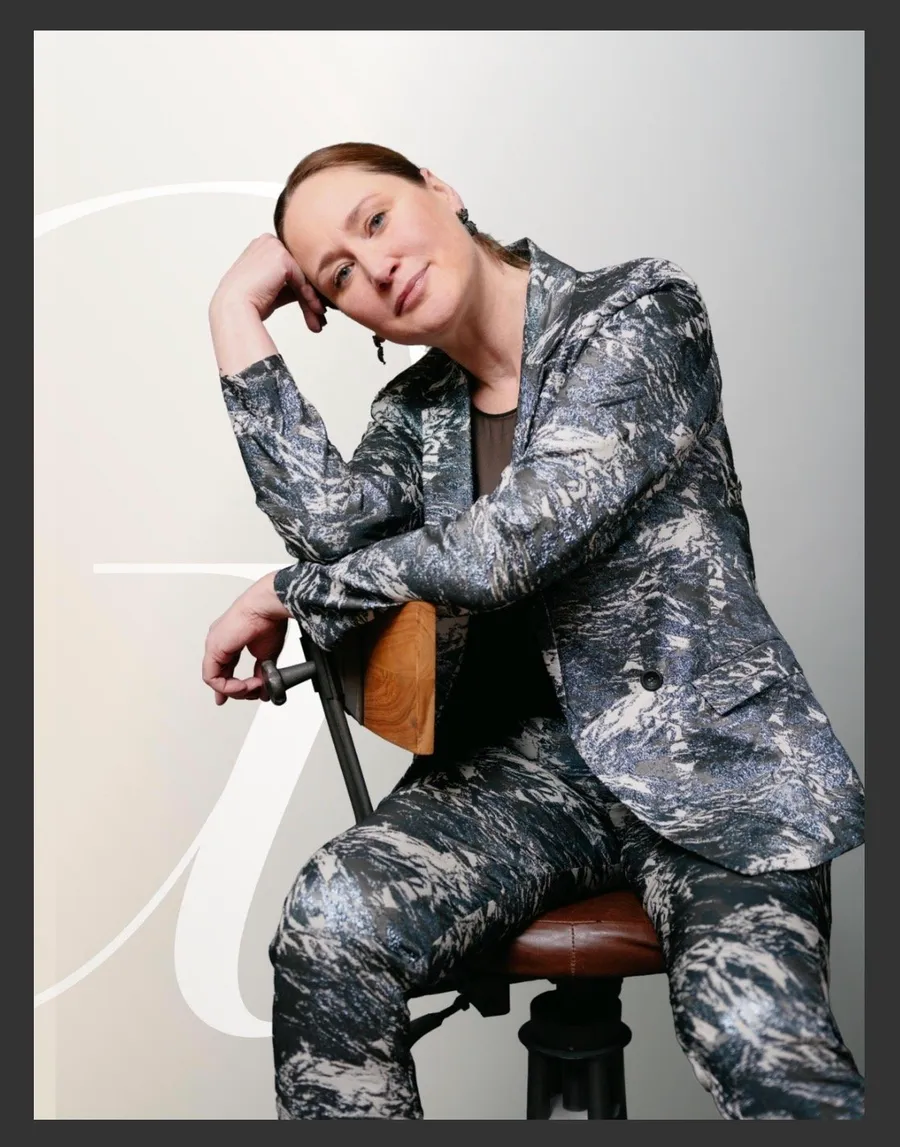 Page de magazine : femme en tailleur à motif argenté assise sur un tabouret, tête appuyée sur la main